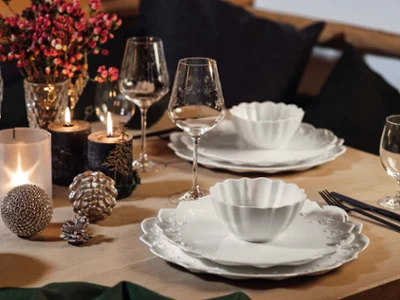 Plato Toy's Delight Royal Classic en una mesa rústica de Navidad Una mesa de comedor con platos blancos Toy's Delight Royal Classic, copas de vino, velas y adornos decorativos. En la mesa también hay flores y una botella de vino tinto.