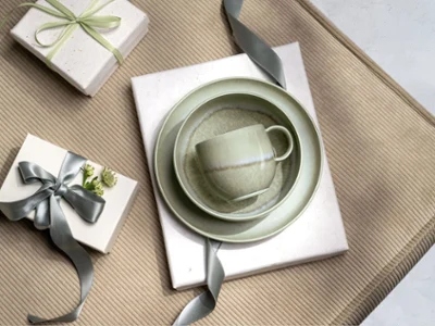 A green Perlemor cup, bowl and plate in a gift box A green Perlemor cup, bowl and plate on gifts wrapped with grey ribbons, arranged on a beige textured surface.