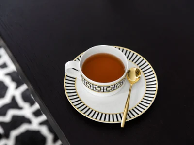 A MetroChic teacup with a gold spoon on a matching saucer. A MetroChic teacup with a gold spoon on a matching saucer, placed on a dark wooden table.