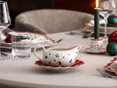 A festive table setting with Villeroy & Boch Toy’s Delight Christmas crockery including a gravy boat, together with wine glasses and a lit candle.