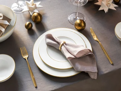 Table élégante avec des assiettes blanches et des couverts dorés Table élégante composée d'assiettes blanches, de couverts dorés, d'une serviette beige avec un anneau, d'ornements décoratifs et de cadeaux emballés sur une nappe grise.