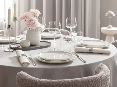 Tavolo da pranzo rotondo con piatti bianchi Afina, bicchieri Afina, posate, tovaglioli e un vaso con fiori rosa.