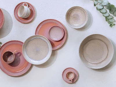 Différentes assiettes et tasses de la collection Perlemor de like. de Villeroy & Boch disposées sur une nappe de blanche.