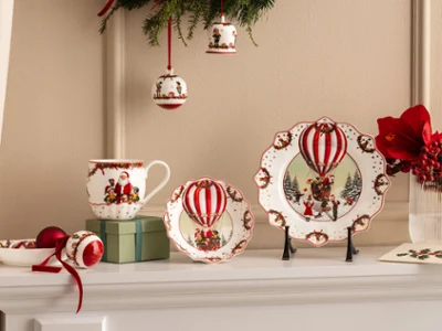 Annual Chistmas edition 2026 collection Festive ceramic plates, cups, and bowls with motifs of red hot air balloons from Villeroy & Boch are presented together with red flowers and Christmas decorations.