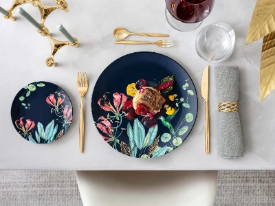 Elegant dining table with Avarua plates and a gourmet dish, accompanied by golden MetroChic flatware and a glass of red wine.