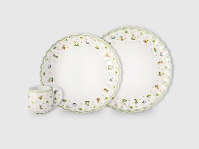 An arrangement of two plates of different sizes and a cup, decorated with green, spring-like accessories, presented on a light background.