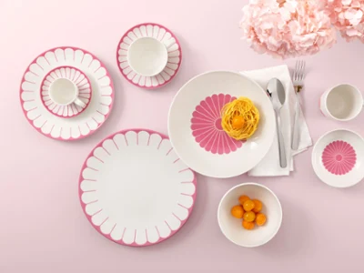 Table setting with Villeroy & Boch Fleur Cassis plates Table setting with Villeroy & Boch Fleur Cassis plates, pasta, clementines, and flowers on a pink background.