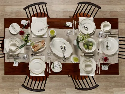 A top view of a wooden dining table set for six people with white crockery from the Villeroy & Boch Manoir collection, along with cutlery, glassware, green accents, bread and place cards on a beige table runner.