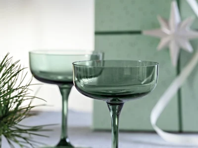 Like Sage glass ideal as a gift Two green cocktail glasses on a white surface with a green gift box and fir branches in the background.