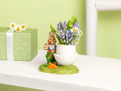 Decorative egg cup plate from the Annual Easter Edition 2024 with an egg shell and spring flowers, displayed on a shelf.