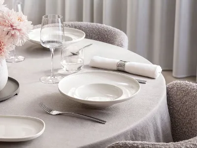 Elegantes Tischarrangement mit tiefen Afina-Porzellantellern sowie passenden Weißwein- und Wassergläsern. Lichtdurchflutete Atmosphäre in einem modernen Ambiente.
