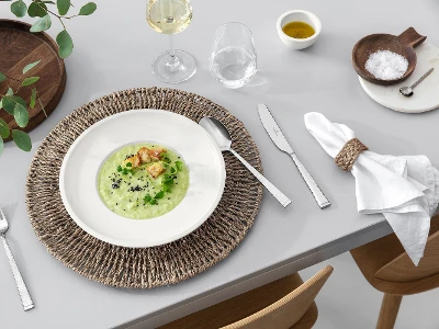 A dining table with Blacksmith flatware, an Artesano dish filled with soup, a glass of white wine and rustic table decorations.