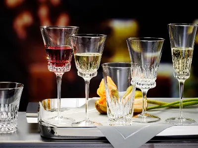 A selection of Villeroy & Boch Grand Royal crystal glasses, each containing a different drink, artfully arranged on a silver tray next to a folded napkin and an orange tulip.