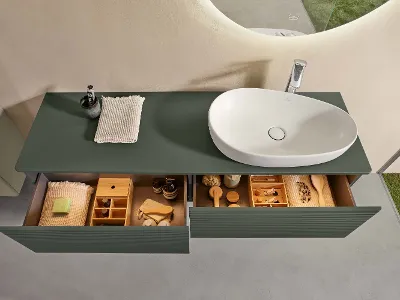 Une console d’un vert naturel dans la salle de bains avec deux tiroirs ouverts et remplis, surmontée d’une vasque blanche Antao de Villeroy & Boch.