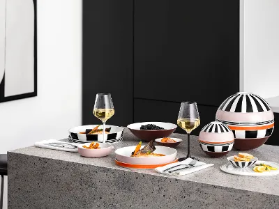 Un tavolo moderno con La Boule e La petite Boule a fantasia, bicchieri da vino e snack su un piano di lavoro grigio in una cucina minimalista.