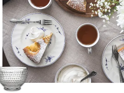 Table set with coffee, whipped cream and plates with fruit cake. Decorative tableware and flowers can be seen.
