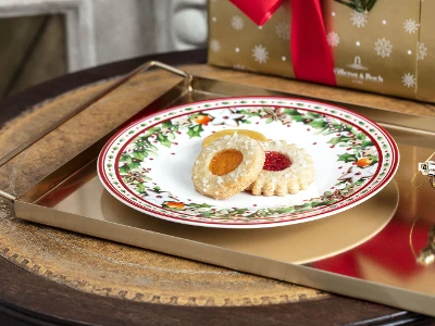 Christmas cookies on a festive Winter Bakery Delight plate with a gift in the background.