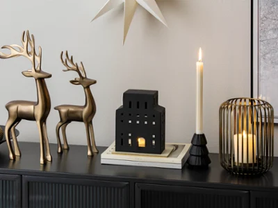 Two metal reindeer, candle holders Zwei metallene Rentiere, Kerzenhalter und eine schwarze, hausförmige Laterne auf einer schwarzen Anrichte.