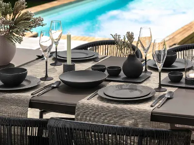 Elegante zona pranzo all'aperto con stoviglie e bicchieri neri della collezione Manufacture a bordo piscina.