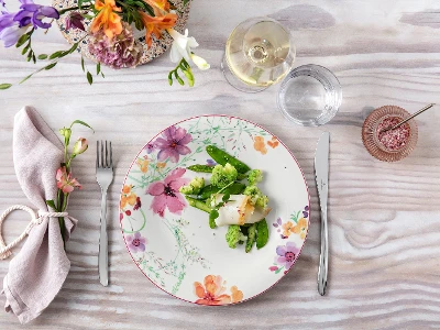 Elegante tavolo da pranzo con un piatto Mariefleur con motivo floreale, un pasto sano e un bicchiere di vino bianco.