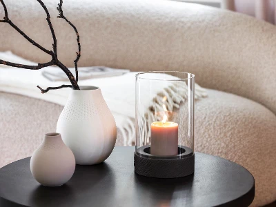 A Manufacture candle stands on a table next to two Manufacture vases.