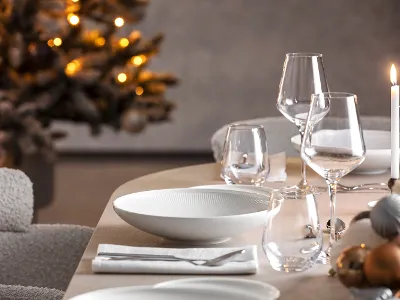 A set dining table with glasses and Afina plates, next to it a burning candle and a decorated Christmas tree in the background.