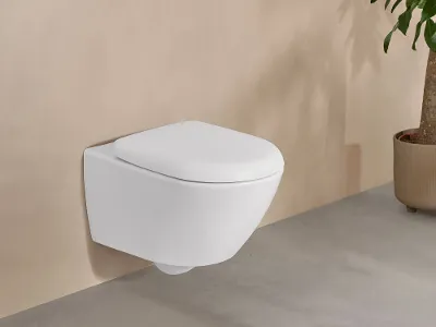 Des toilettes blanches Antao de Villeroy & Boch dans une élégante salle de bains beige avec une plante en pot.