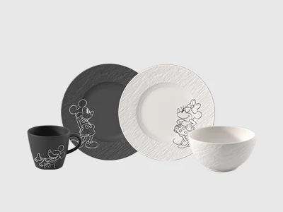 An arrangement of two plates of same sizes and a cup and a bowl, Mickey Mouse and Mini Mouse, presented on a light background.