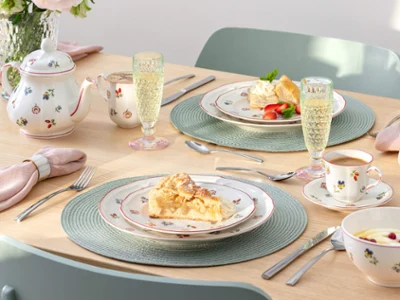 Petite Fleur como juego floral de café y tarta Una mesa puesta para dos personas con platos de postre, tazas de té, una tetera, copas de champán y porcelana con estampados florales de Petite Fleur.