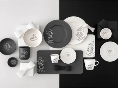 Toute la collection Manufacture Mickey avec des assiettes, tasses et bols noirs et blancs sur un fond noir et blanc divisé.
