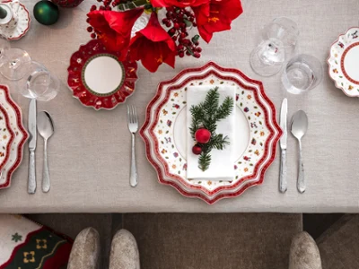 Top view of an elegant festive table with the Villeroy & Boch Toy's Delight collection, complete with red and white plates, silver cutlery and a festive napkin decorated with pine wood and ornaments.