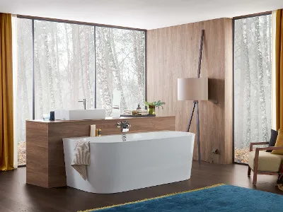 Une salle de bains moderne avec une baignoire en îlot blanche, des boiseries, un grand plan de toilette, des fenêtres du sol au plafond avec des rideaux jaunes, un fauteuil et un tapis bleu.