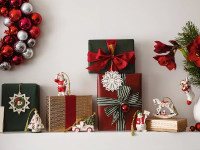 Festive Christmas shelf with wrapped presents, Christmas decorations from Villeroy and Boch, a wreath with red and silver ornaments from Villeroy and Boch and a vase with red flowers and green plants.