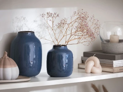 Two blue Lave vases stand on a shelf next to a decorative porcelain pumpkin.