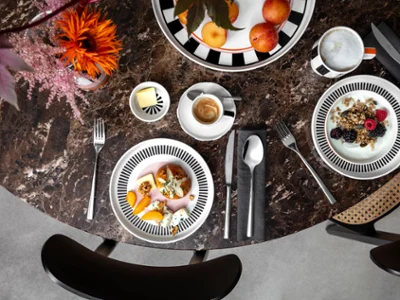 Vista dall'alto di un tavolo di marmo con ciotole di frutta, caffè, cereali e yogurt della collezione Memphis di Villeroy & Boch, posate e decorazioni floreali.