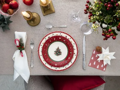 Table set for a banquet with red and white plates, cutlery, candles and festive decorations, seen from above.