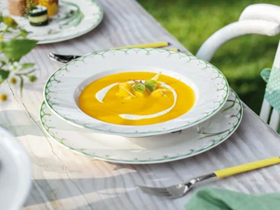 Colourful Spring soup plate with sweet potato and mango soup A Colourful Spring soup plate with sweet potato and mango soup, garnished with herbs and cream, stands on a decorative wooden table with a fork next to it.