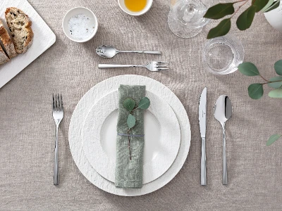 Une table dressée avec des assiettes Manufacture blanches de Villeroy & Boch ainsi que des feuilles d’eucalyptus et des couverts de table.