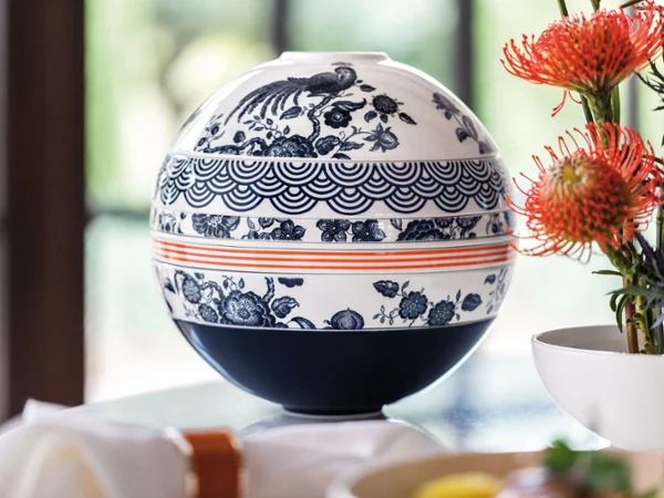 There is a La Boule Paradiso in blue and white on a table next to flowers.