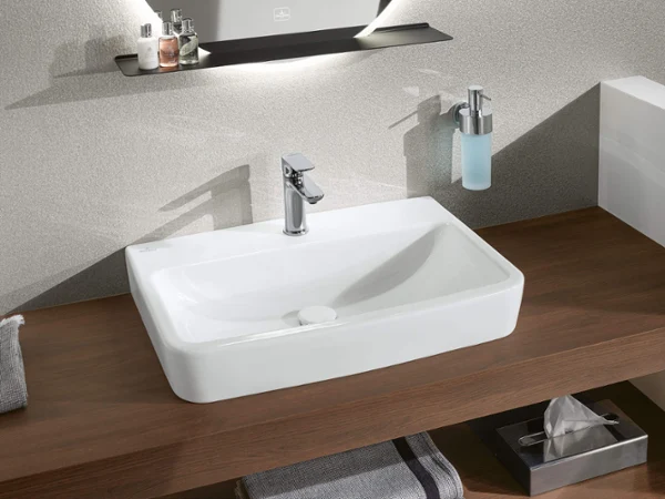 Rectangular white washbasin with a silver tap on a wooden worktop, with a soap dispenser on the wall above.