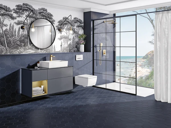 Une salle de bains exclusive avec du carrelage en nid d’abeilles bleu foncé et du papier peint représentant des palmiers, des WC Memento 2.0 blancs, une douche ouverte avec paroi vitrée et une grande fenêtre offrant une vue sur la mer. 