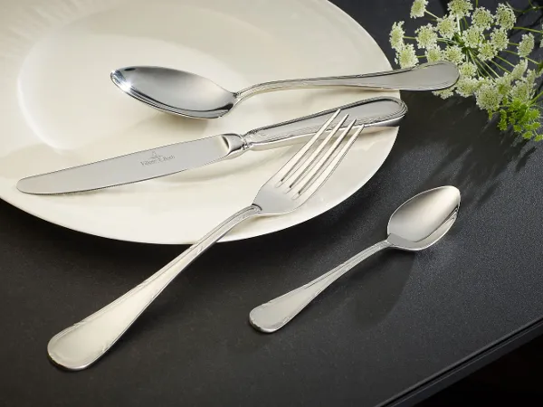 Une assiette blanche avec des couverts de table de la collection Kreuzband Septfontaine sur une surface noire.