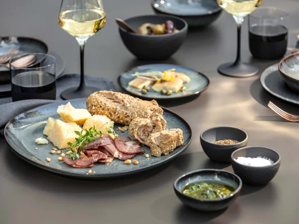 Manufacture with Lave Gris Charcuterie Table Setting Modern table setting featuring Manufacture and Lave Gris stoneware with charcuterie, artisan bread, wine, dipping bowls, and black glassware on a dark dining table.