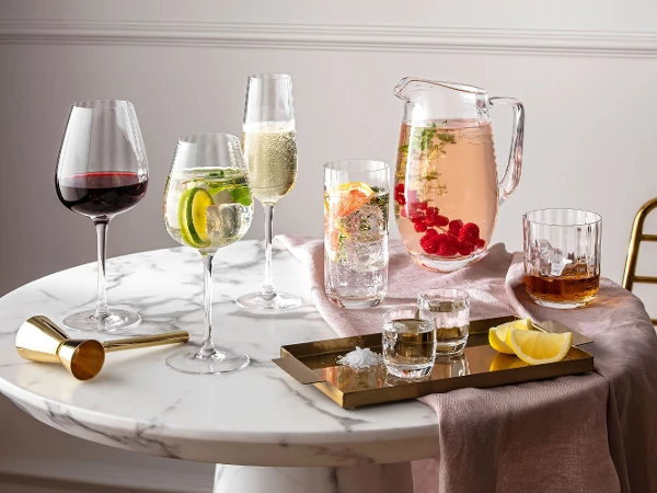 Glazen en kannen uit de Rose Garden collectie van Villeroy & Boch op een ronde marmeren tafel met drankjes en citrusvruchten.