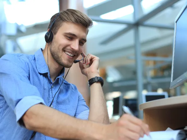 Homme souriant avec un casque travaillant sur un ordinateur dans un environnement de bureau.