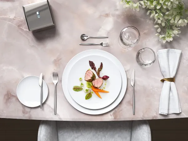 Stilig marmorbord med gourmetretter på hvite MetroChic-tallerkener, ledsaget av MetroChic-bestikk og blomsterdekorasjon.