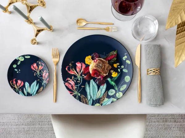 Un table de salle à manger élégante avec des assiettes Avarua et un plat gastronomique, le tout accompagné de couverts de table MetroChic dorés et d’un verre de vin rouge.