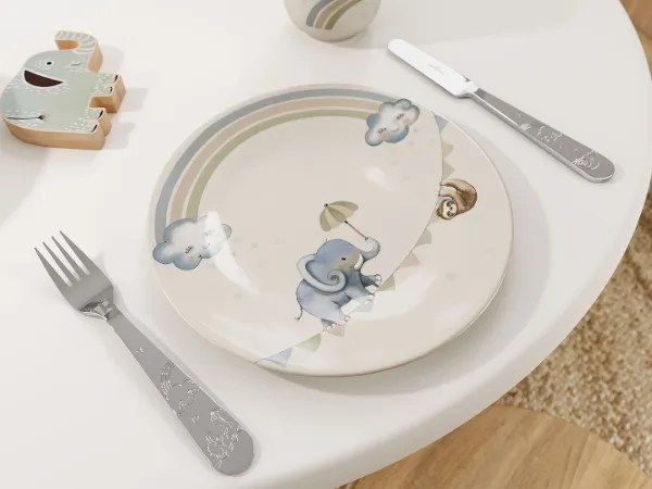 Der Kinderteller Boho Kids | Walk like an Elephant von Villeroy & Boch zeigt ein Elefantendesign auf einem Tisch mit Gabel und Messer, ergänzt durch eine Spielfigur in Elefantenform im Hintergrund.