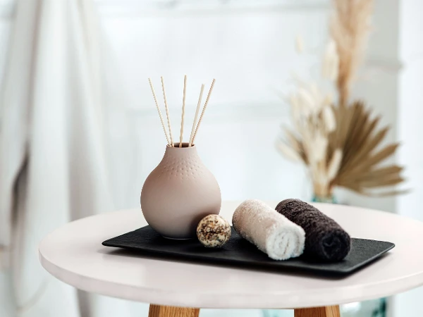 Beige Manufacture Vase mit Duftstäbchen auf einem Tablett mit Handtüchern.