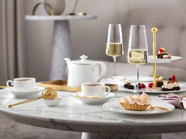 Elegantes Nachmittagstee-Setup mit Desserts und Champagner auf einem Marmortisch, serviert auf Château Septfontaines Geschirr und MetroChic Gläsern.